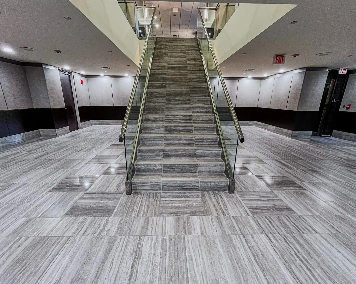 Commercial lobby staircase with glass railings and stone-look flooring