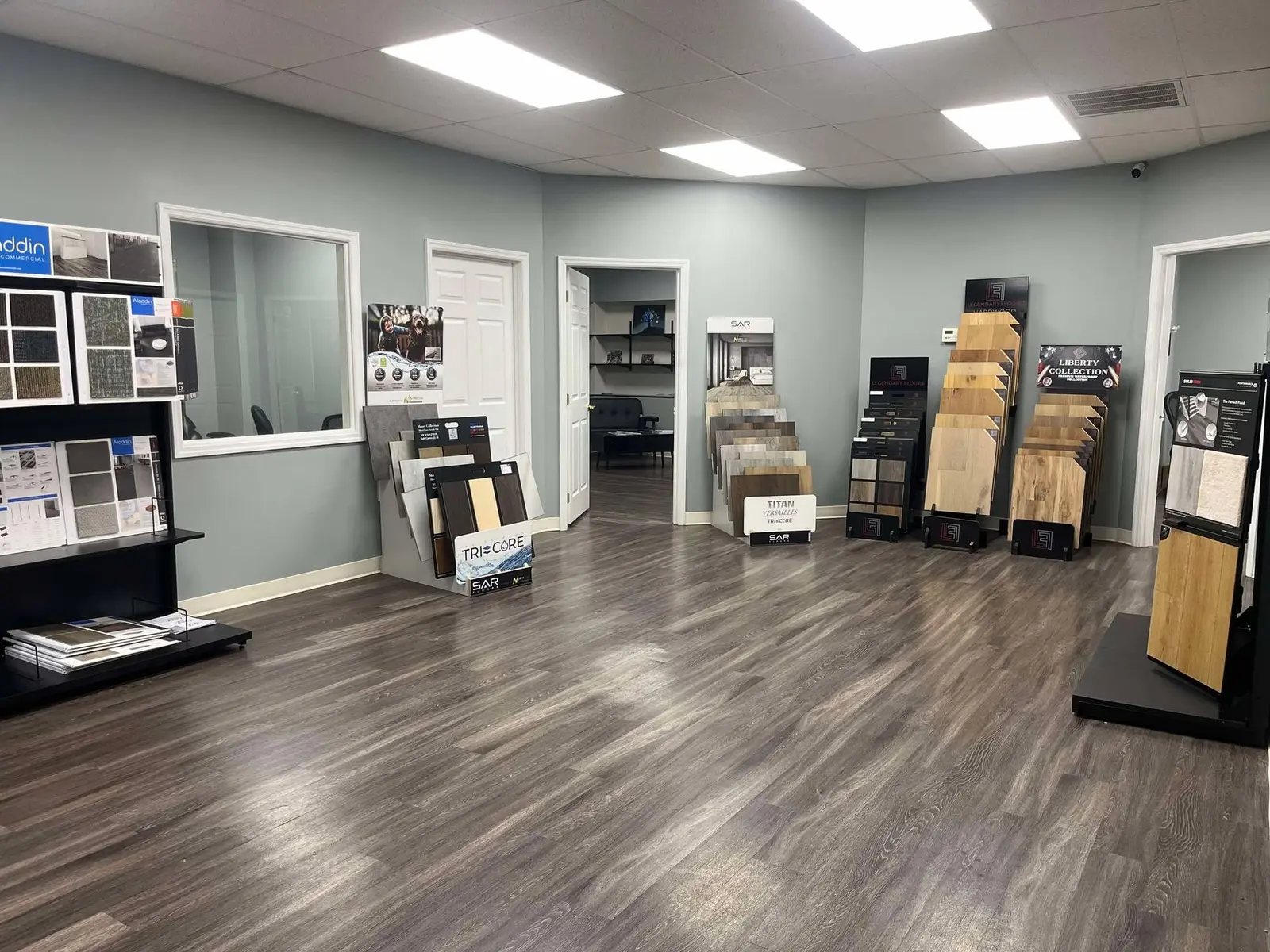 Showroom sample racks from SAR Floors, Legendary Floors, and Liberty Collection on a wood-look floor